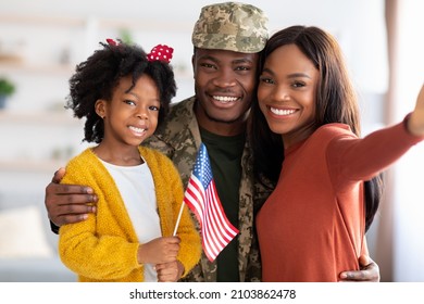 Happy American Soldier Taking Selfie With Family After Returning Home From Army, Black Man In Military Uniform Posing At Camera With Wife And Little Daughter Holding USA Flag, Closeup Shot, POV - Powered by Shutterstock