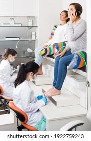 Happy American Woman Relaxing In Nail Salon On Pedicure And Using Phone.