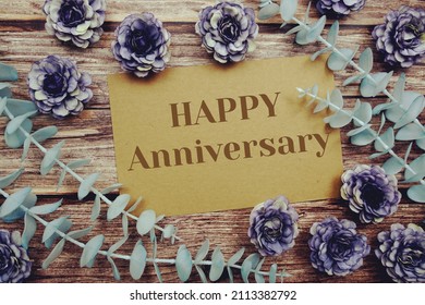 Happy Anniversary typography text on paper card decorate with flower on wooden background