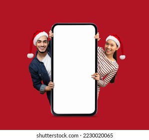 Happy arab and asian young lady and guy in Santa Claus hats peeking out from big smartphone with empty screen isolated on red background. Digital offer, ad and app, New Year and Christmas holiday - Powered by Shutterstock