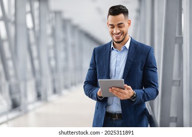 Happy Arab Businessman Booking Hotel Online While Using Digital Tablet In Airport, Handsome Middle Eastern Entrepreneur With Tab Computer Standing In Terminal, Waiting For Flight Boarding, Copy Space