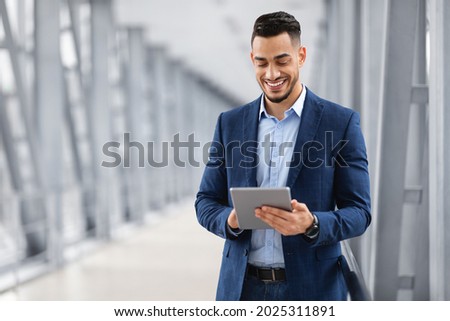 Happy Arab Businessman Booking Hotel Online While Using Digital Tablet In Airport, Handsome Middle Eastern Entrepreneur With Tab Computer Standing In Terminal, Waiting For Flight Boarding, Copy Space