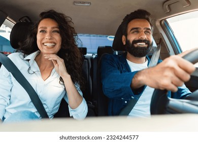 Happy arab couple going on summer vacation by car, man and woman sitting in their new auto, cheerfully smiling looking at road, making test drive in the city - Powered by Shutterstock