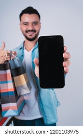 Happy Arab Man Holding Shopping Bags And Showing Mobile Screen