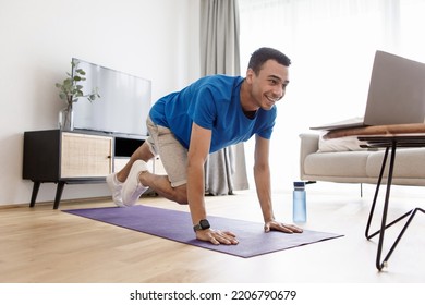 Happy Arab Man In Sportswear Exercising At Home In Front Of Laptop, Watching Fitness Video On Internet Or Having Online Fitness Class, Living Room Interior, Copy Space