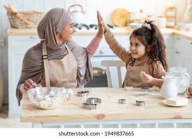 Happy Arab Mom Giving High Five To Her Little Daughter While Baking In Kitchen, Cute Preschool Girl Having Fun With Muslim Mommy At Home, Enjoying Cooking Together With Mother, Closeup