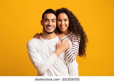 Happy Arab Spouses. Closeup Portrait Of Cheerful Middle Eastern Couple Hugging And Smiling At Camera, Joyful Millennial Lovers Standing Over Yellow Background, Posing Together In Studio, Copy Space