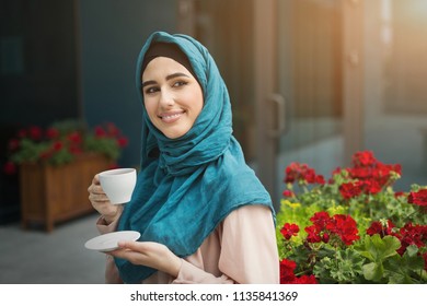 Happy arab woman in hijab drinking coffee in cafe outdoors, copy space - Powered by Shutterstock