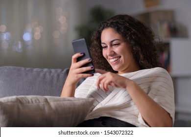 Happy Arab Woman Using Smart Phone Sitting On A Couch In The Night At Home