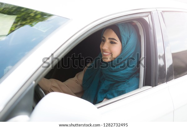 Happy arabian lady wearing hijab driving her new\
car. Modern arabic woman\
concept