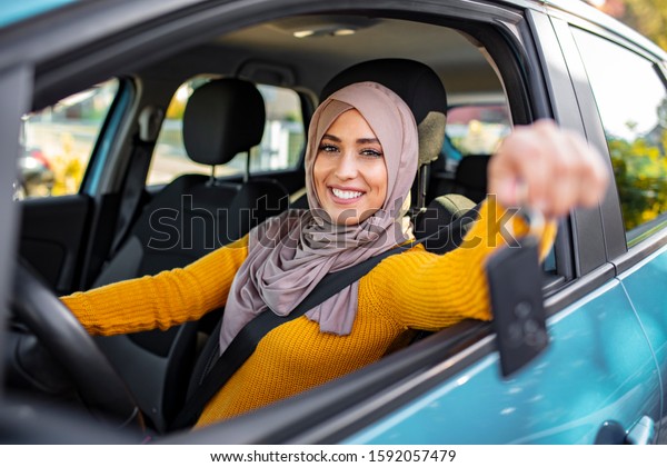 Happy arabian woman holding\
car key in new vehicle. Muslim woman in her new car. Happy arabian\
woman holding car key inside new vehicle. Muslim Woman Sitting In\
Car