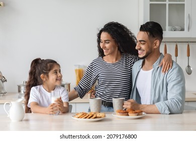 Happy arabic family having breakfast while spending weekend together at home, cheerful young father, mother and curly little girl sitting at kitchen, drinking coffee and milk with homemade cookies - Powered by Shutterstock