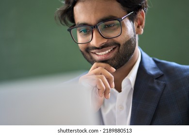 Happy Arabic Indian Young Business Man Executive Professional Financial Manager, Office Employee Wearing Suit And Glasses Working On Laptop Looking At Computer Checking Online Data Tech Management.