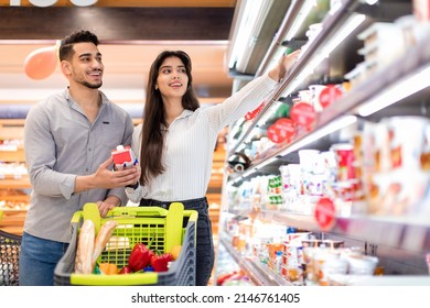 Happy Arabic Spouses Buying Food And Dairy Products During Grocery Shopping Holding Milk Standing Near Shelf In Modern Supermarket. Happy Customers Purchasing Essentials In Store - Powered by Shutterstock