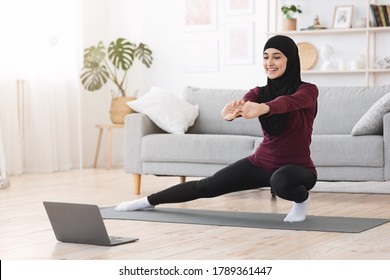 Happy Arabic Woman In Hijab Doing Lunges In Front Of Laptop At Home, Making Fitness Training Via Online Tutorials, Copy Space