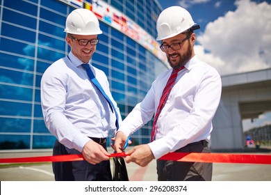 Happy architect cutting red ribbon at official opening of new construction 