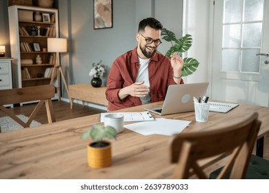 Happy architect gesturing while engaging in video conferencing on a laptop at a home office, working remotely and participating in an online meeting with clients and colleagues