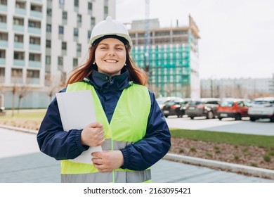 Happy Architect with paper folder with documents at a construction site. Portrait of successful woman constructor wearing white helmet and safety yellow vest. Woman are planning new building project.