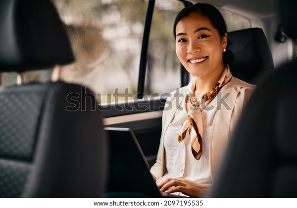Happy Asia female CEO\
sitting in the backseat and working on laptop while going on a\
business trip by car.