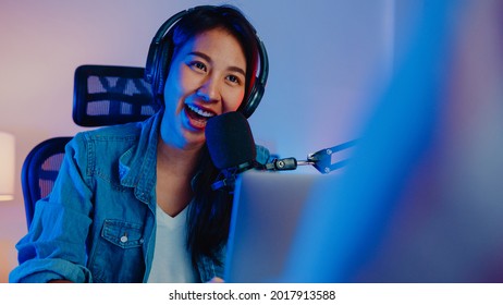 Happy asia girl host record podcast use microphone wear headphone with laptop interview guest conversation for content in her home studio at night. Sound equipment concept. Content creator concept. - Shutterstock ID 2017913588