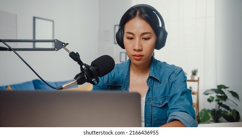 Happy Asia Girl Record A Podcast On Laptop Computer With Headphones And Microphone Talk With Audience At Living Room. Female Podcaster Make Audio Podcast From Her Home Studio. Stay At House Concept.