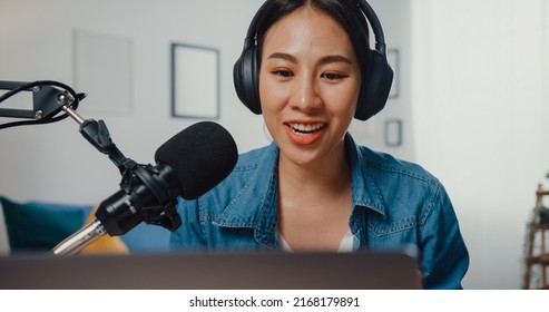 Happy Asia Girl Record A Podcast On Laptop Computer With Headphones And Microphone Talk With Audience At Living Room. Female Podcaster Make Audio Podcast From Her Home Studio. Stay At House Concept.