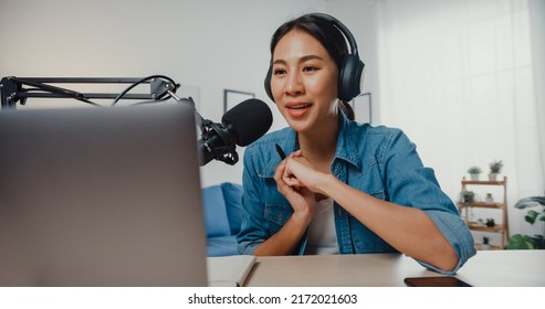 Happy Asia Girl Record A Podcast On Laptop Computer With Headphones And Microphone Talk With Audience At Living Room. Female Podcaster Make Audio Podcast From Her Home Studio. Stay At House Concept.