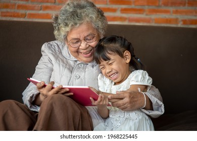 Happy Asia Grandmother Reading To Granddaughter Child Book At Home,Grandmother Teaches To Read A Book Her Granddaughter.