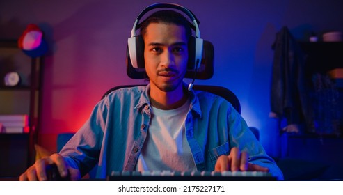 Happy asia guy gamer wear headphone participation play video game colorful neon lights computer in living room at night modern house. Esport streaming game online, Home quarantine activity concept. - Shutterstock ID 2175227171