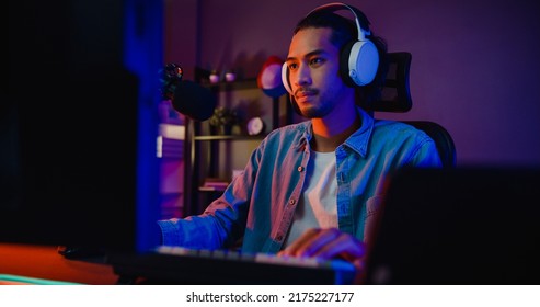 Happy asia guy gamer wear headphone participation play video game colorful neon lights computer in living room at night modern house. Esport streaming game online, Home quarantine activity concept. - Powered by Shutterstock