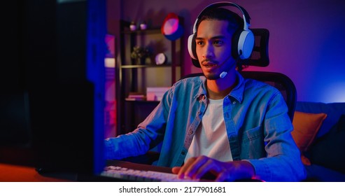 Happy asia guy gamer wear headphone participation play video game colorful neon lights computer in living room at night modern house. Esport streaming game online, Home quarantine activity concept. - Shutterstock ID 2177901681
