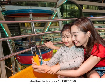 Happy Asia Mother And Daughter Have Fun Selfie Sitting In Gondola Of Ferris Wheel Amusement Park At Night