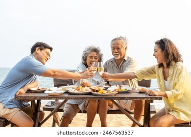 Happy Asian adult couple and aging parents enjoy outdoor lifestyle celebration dinner party drinking champagne together at tropical beach restaurant during travel ocean on summer holiday vacation.  - Powered by Shutterstock