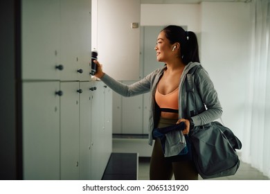 Happy Asian athletic woman taking her stuff from a locker after finishing sports training in a gym.