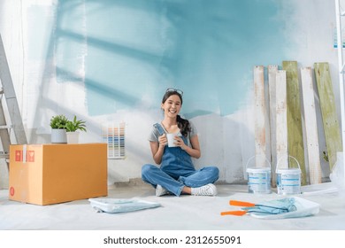 Happy Asian attractive young woman having coffee break during home renovation her living room. Woman repairman painted the wall with paint makes repairs and sits on a floor home relocation renovate - Powered by Shutterstock