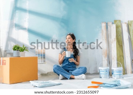 Happy Asian attractive young woman having coffee break during home renovation her living room. Woman repairman painted the wall with paint makes repairs and sits on a floor home relocation renovate Imagine de stoc © 