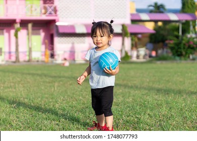 Happy Asian Baby Child Girl Playing And​ Holding A​ Ball Toys At The Field Playground. She Smiling And Wearing A Blue Shirt. Baby Aged Of 2-3 Years Old. Exercise For Health. Sport And Kids Concept.