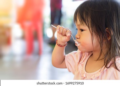 Selective​ Focus​ Of​ Happy Asian Baby Child Girl​eating Yogurt Food By Herself. Her Face Is Sloppy And Messy. 2-3​ Years​ Old​ Baby.​ Kid And Food Concept.