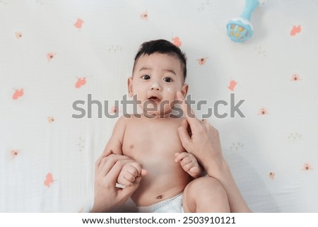 Happy Asian Baby with a Comfortable Smile, Mother Finger Gently Applying Skin Care Lotion on His Face. Joyful Moments. Baby care.
