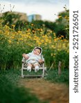 Happy asian baby girl child is sitting on chair smiling in yellow cosmos flowers field summer time, This is a concept of a happy and carefree childhood