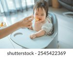 Happy asian baby girl eating first food pumpkin from spoon with mom at home, Meal time, Little girl eats sitting on baby