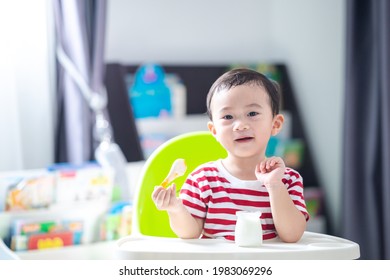 Happy Asian Baby Sitting In A Children Chair Eating Yogurt, Healthy Food Concept.