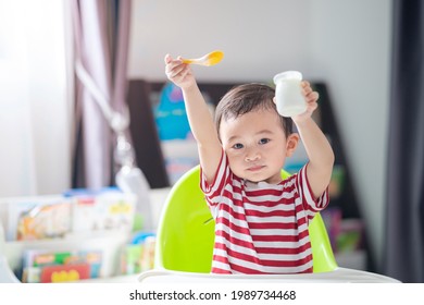 Happy Asian Baby Sitting In A Children Chair Eating Yogurt, Healthy Food Concept.