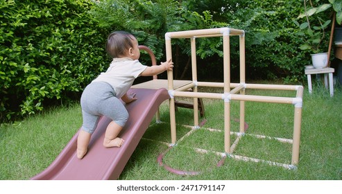 A happy Asian baby toddler child is playing on a slide in a backyard. The baby is crawling up the slide, and the scene is playful and joyful - Powered by Shutterstock