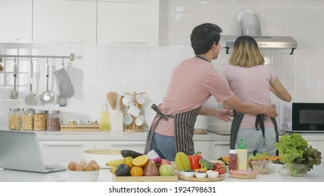 Happy Asian Beautiful Family Couple Husband And Wife Cooking Vegetable Salad In Kitchen Together At Home. The Man Sneaked In To Pretend To Tickle The Waist Woman. Healthy Food Concept