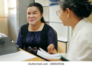 Happy Asian blind person woman with vintage braille typewriter or Brailler for people with vision disabilities, working and talking with senior colleague woman in office workplace.