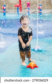 Happy Asian Boy Has Fun Playing In Water Fountains In Water Park