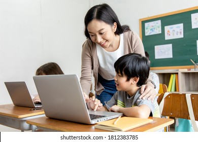 Happy Asian boy learning to code or search internet on laptop with guidance from female teacher. Concept of computer science, digital literacy, STEM education, and modern primary school curriculum.