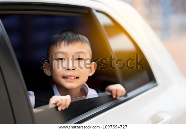 Happy Asian\
boy smiling holding mirror on window of car on uniform school. Cute\
child happy and going to school in morning. He is playful boy and\
learning in primary school\
