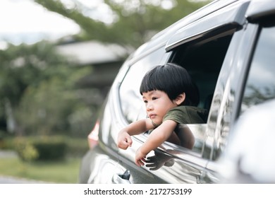 Happy Asian Boy Waving Hands Gesturing Hello Out Of The Car Window During A Trip With His Family. Little Child Sticking Head Outta The Windshield Traveling In A Car On A Summer Vacation.